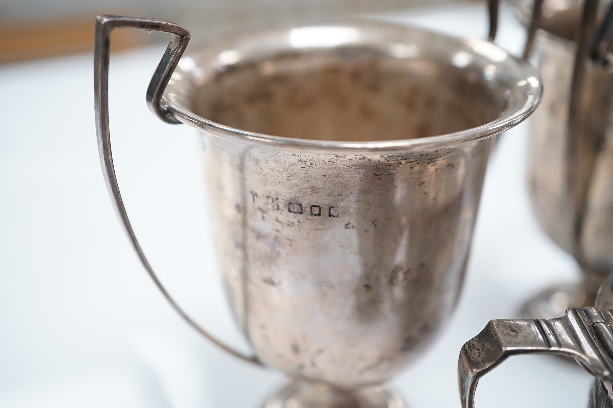 A Victorian repousse silver drum mustard, London, 1887, a silver three piece condiment set, Birmingham, 1936 and a set of three small trophy cups by Mappin & Webb, London, 1925/6. Condition - poor to fair